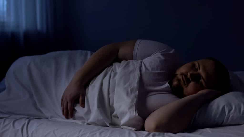 Obese man sleeping in bed, relaxing at night on comfortable mattress