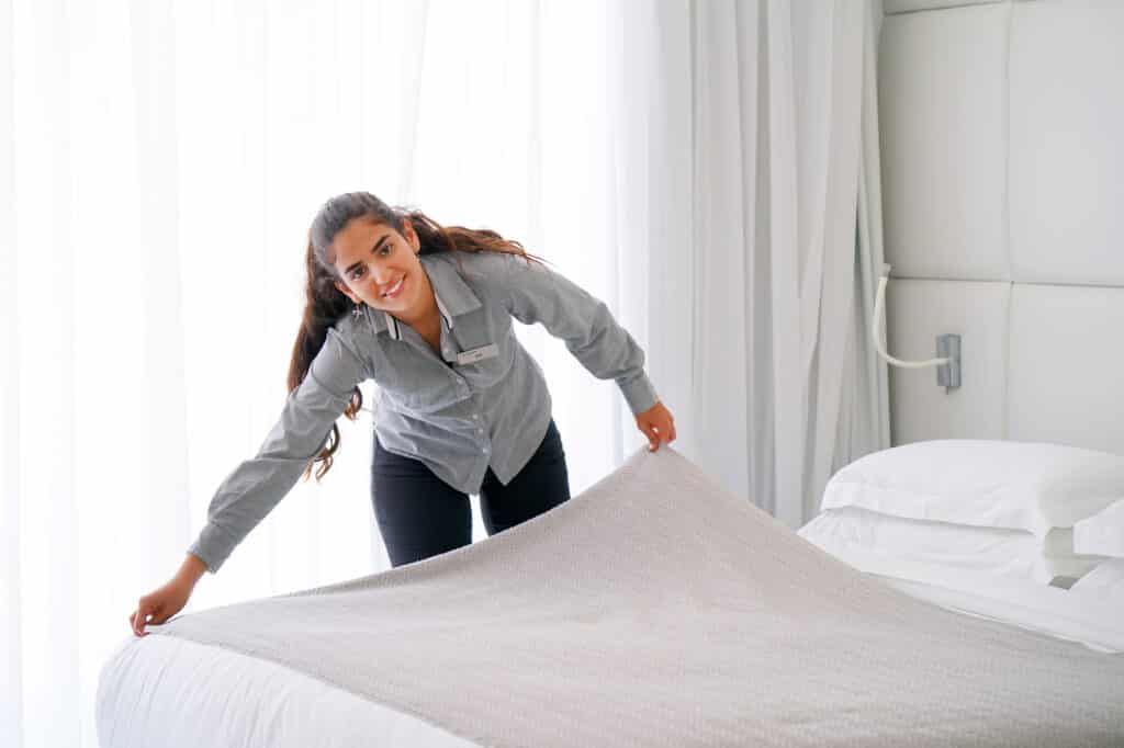 Maid making bed in hotel room.