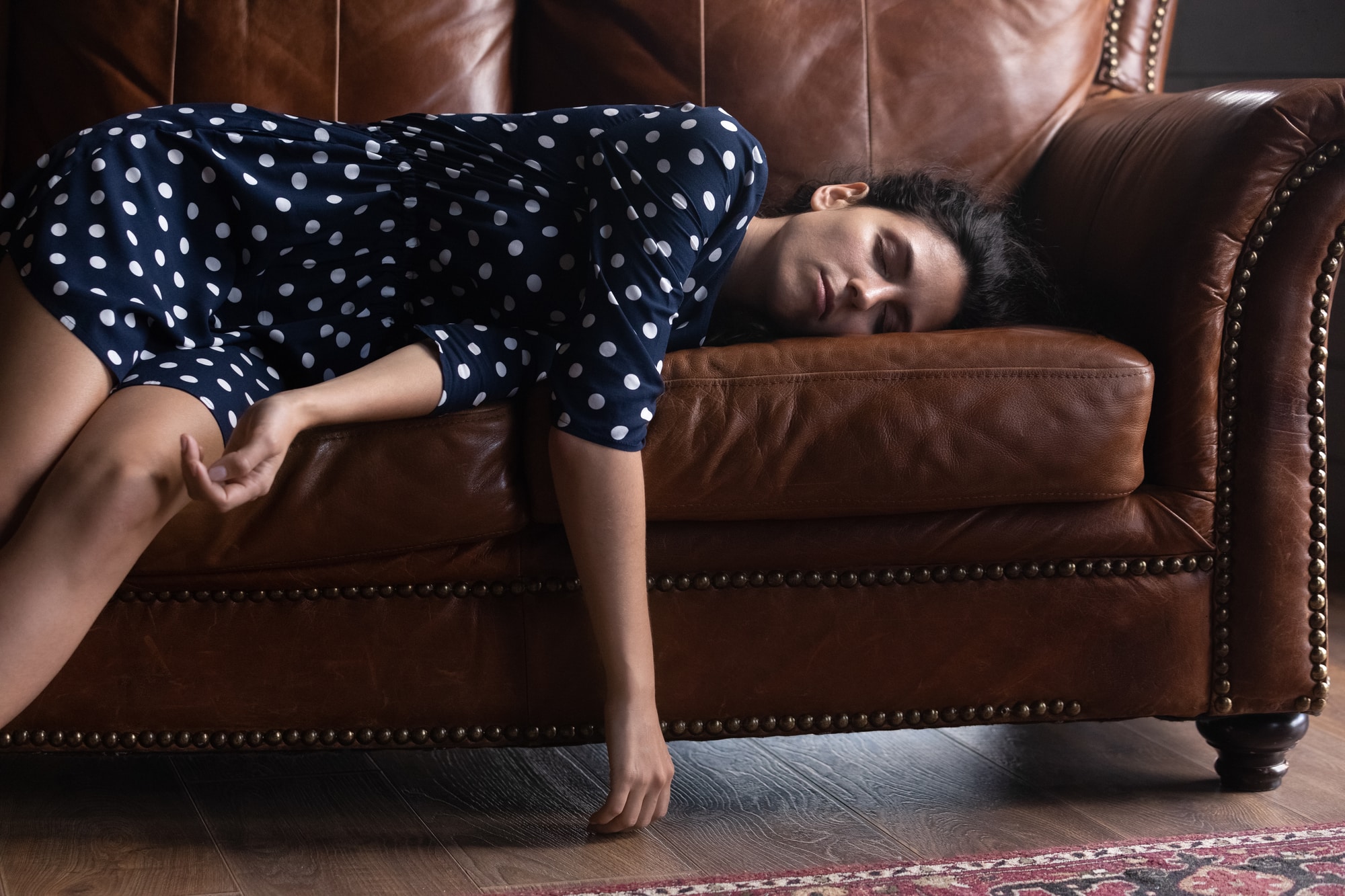 Exhausted Hispanic woman resting on comfortable leather couch