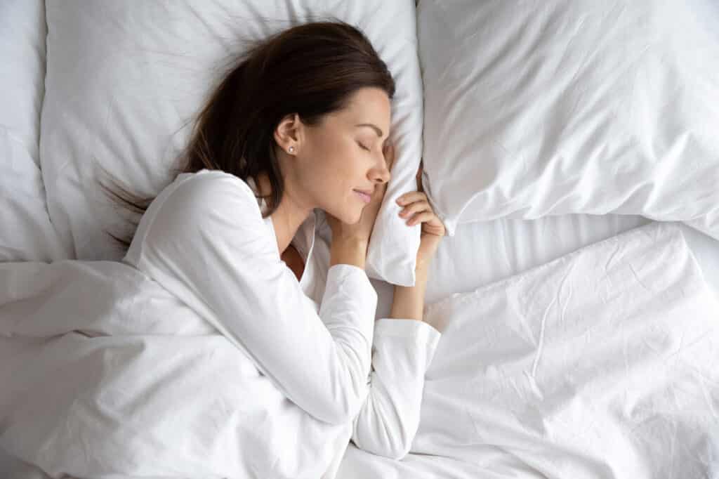 Serene beautiful woman sleeping with hand under cheek on soft pillow